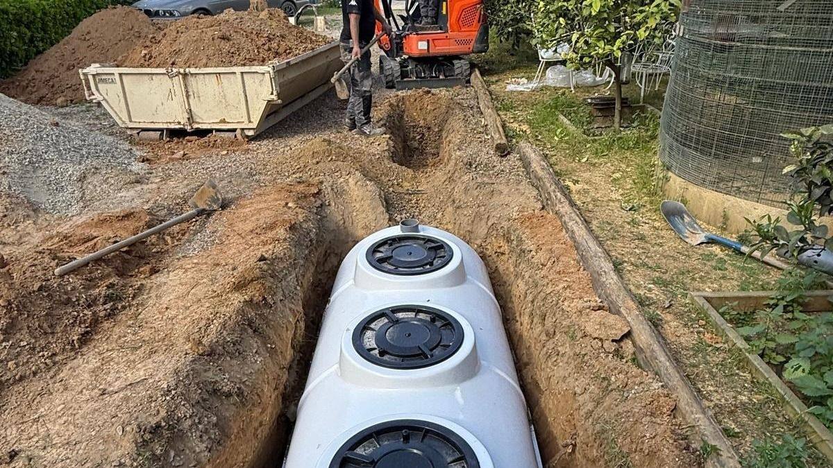 Instalación de una fosa séptica en una casa de campo: zanja abierta, depósito colocado y miniexcavadora retirando la tierra